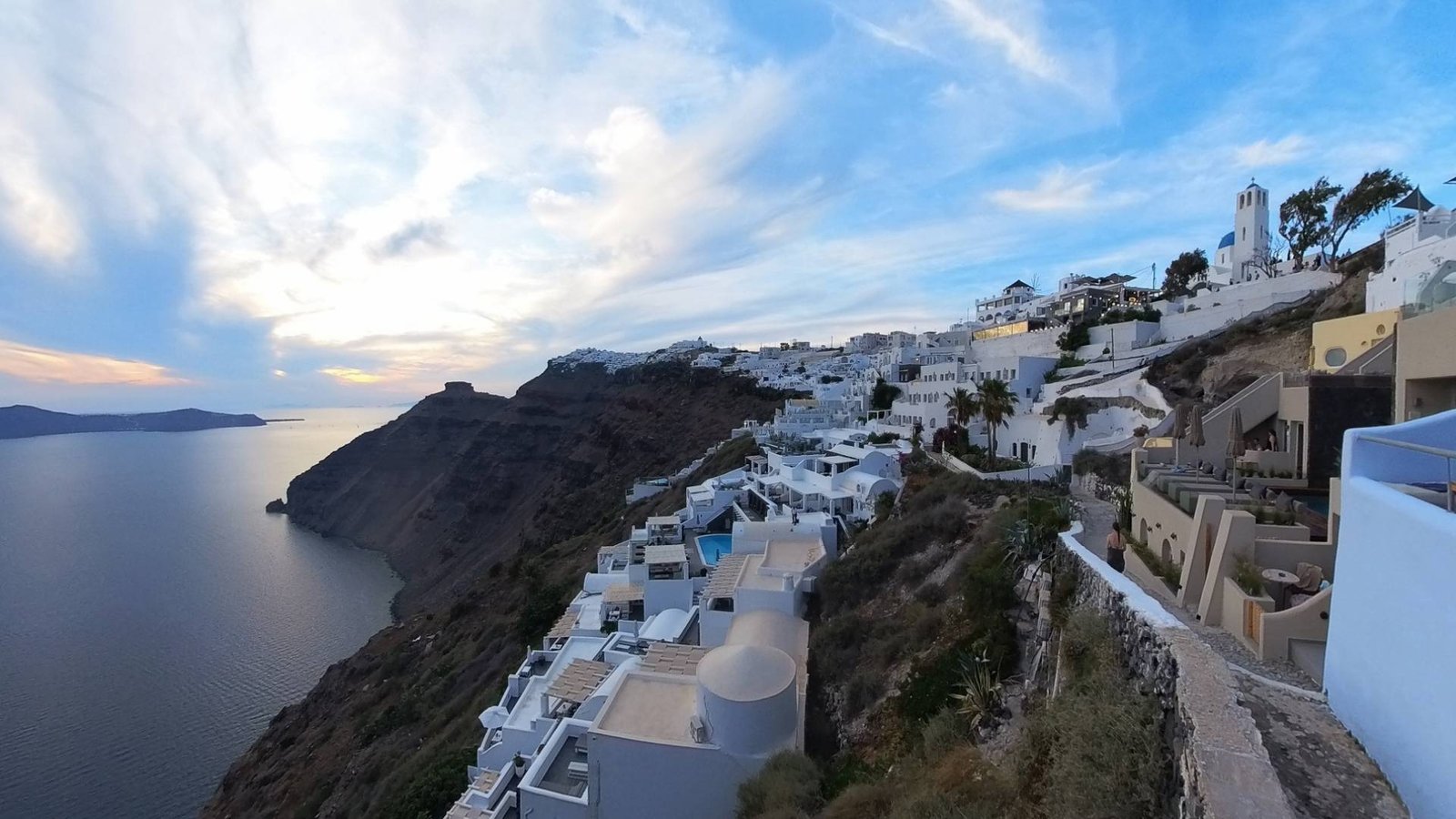Sunset view of Oia village with white houses and blue domes on the caldera cliffs, featured in the Santorini virtual tour.